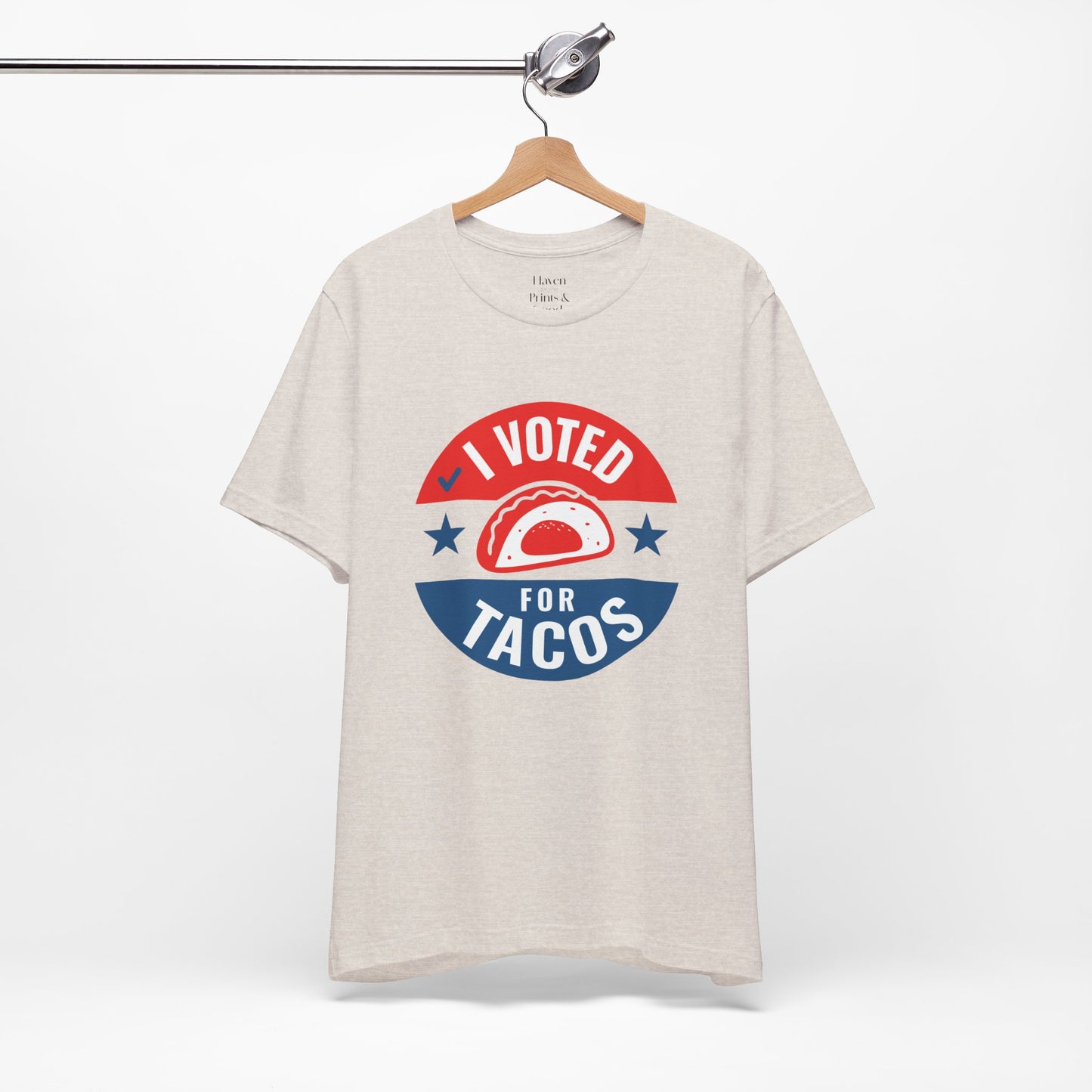 Beige t-shirt with 'I Voted for Tacos' graphic on a hanger against a white background
